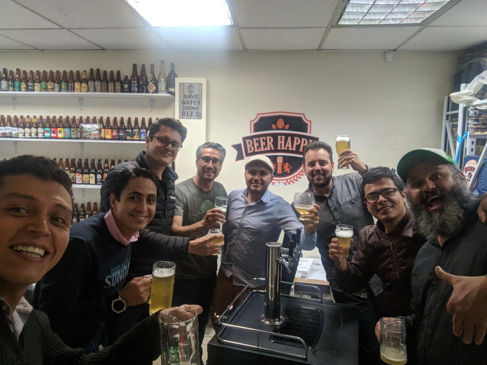 The Beer Happy Club team toasting with craft beer in front of the club logo