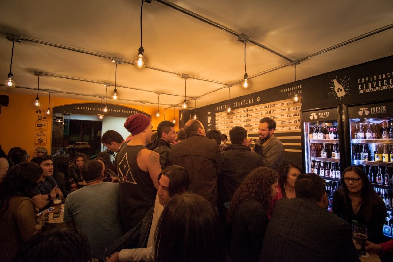 A crowded evening inside Puerto Cervecero, with the beer menu on the wall