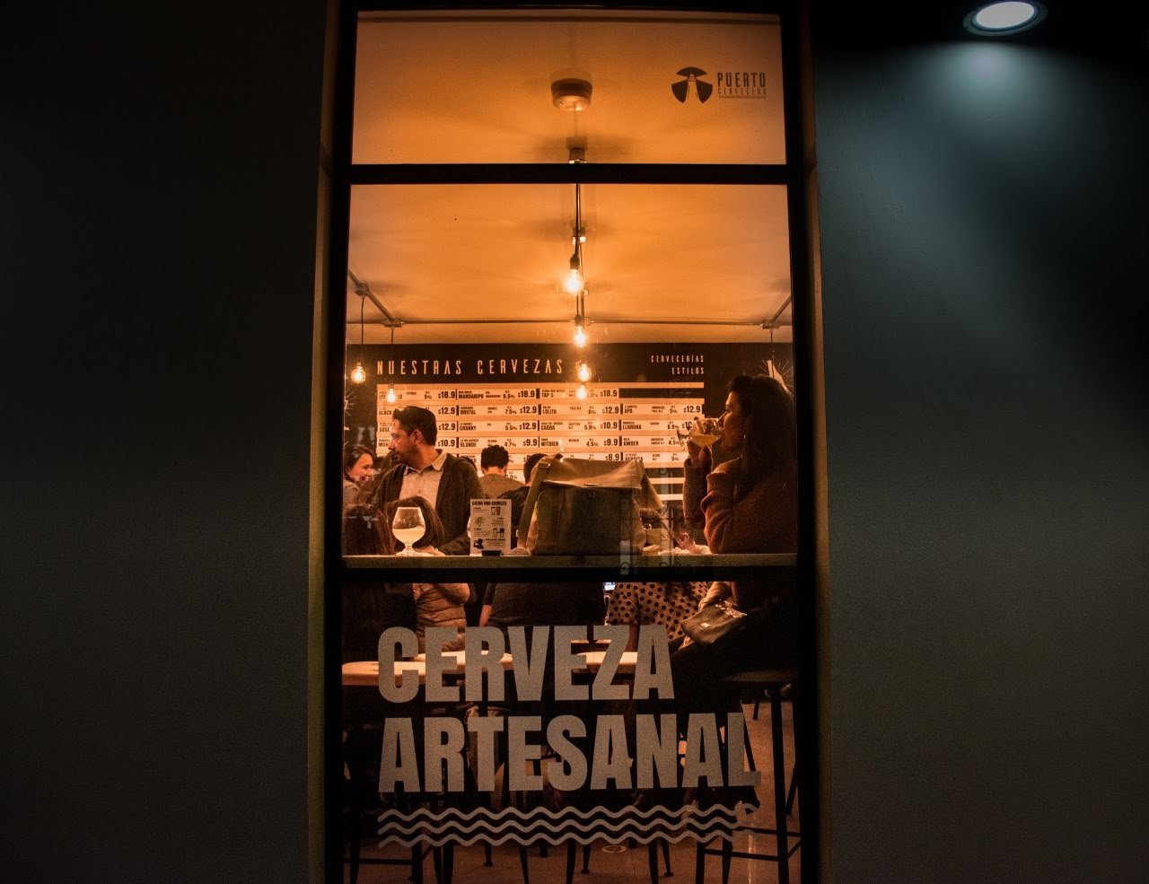 People drinking craft beer, seen through the Puerto Cervecero window